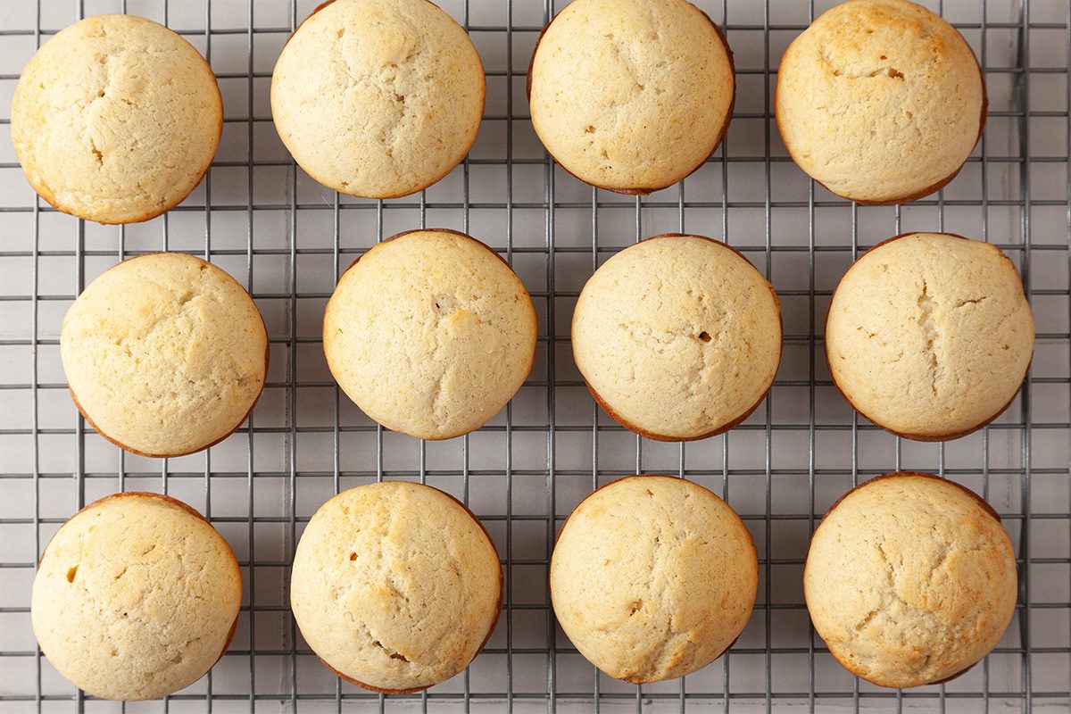 Twelve golden baked muffins are arranged in three rows of four on a cooling rack with a grid pattern.