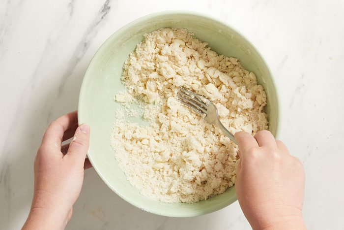 A person holds a bowl of crumbled tofu and mixes it with a fork on a white marble surface.