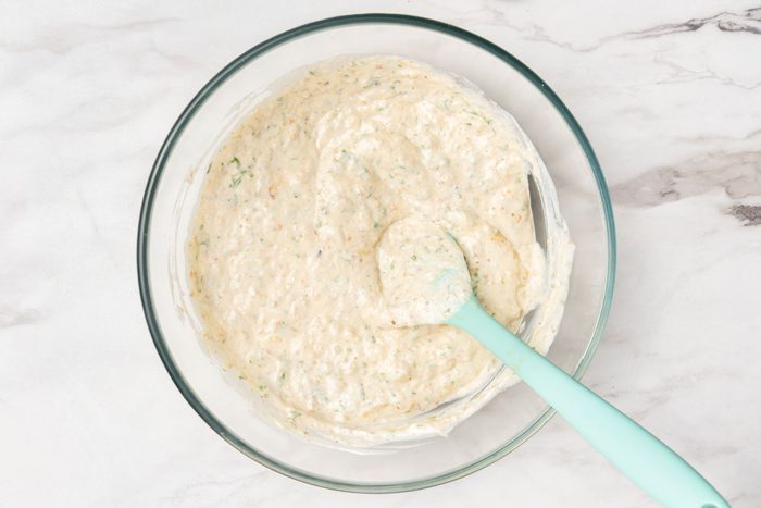 Overhead shot of a glass bowl filled with a creamy, speckled mixture sits on a marble surface; A light blue spatula rests in the bowl, partially covered with the mixture;