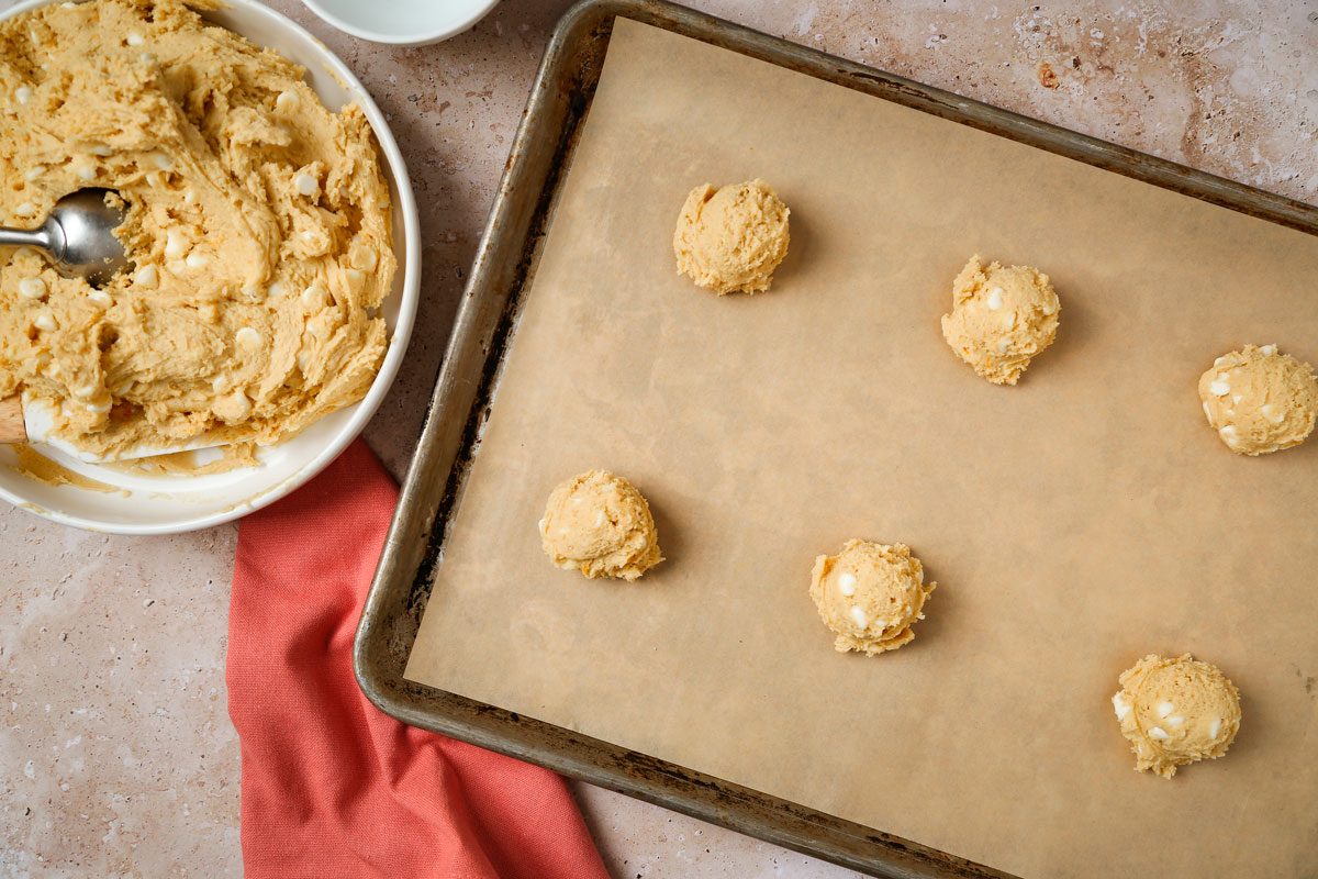 Overhead shot of scoop dough by 1/4 cupfuls 2-inch apart onto greased or parchment-lined baking sheets; orange napkin; Bake until edges are golden brown, 15-17 minutes; all set on a texture marble surface;