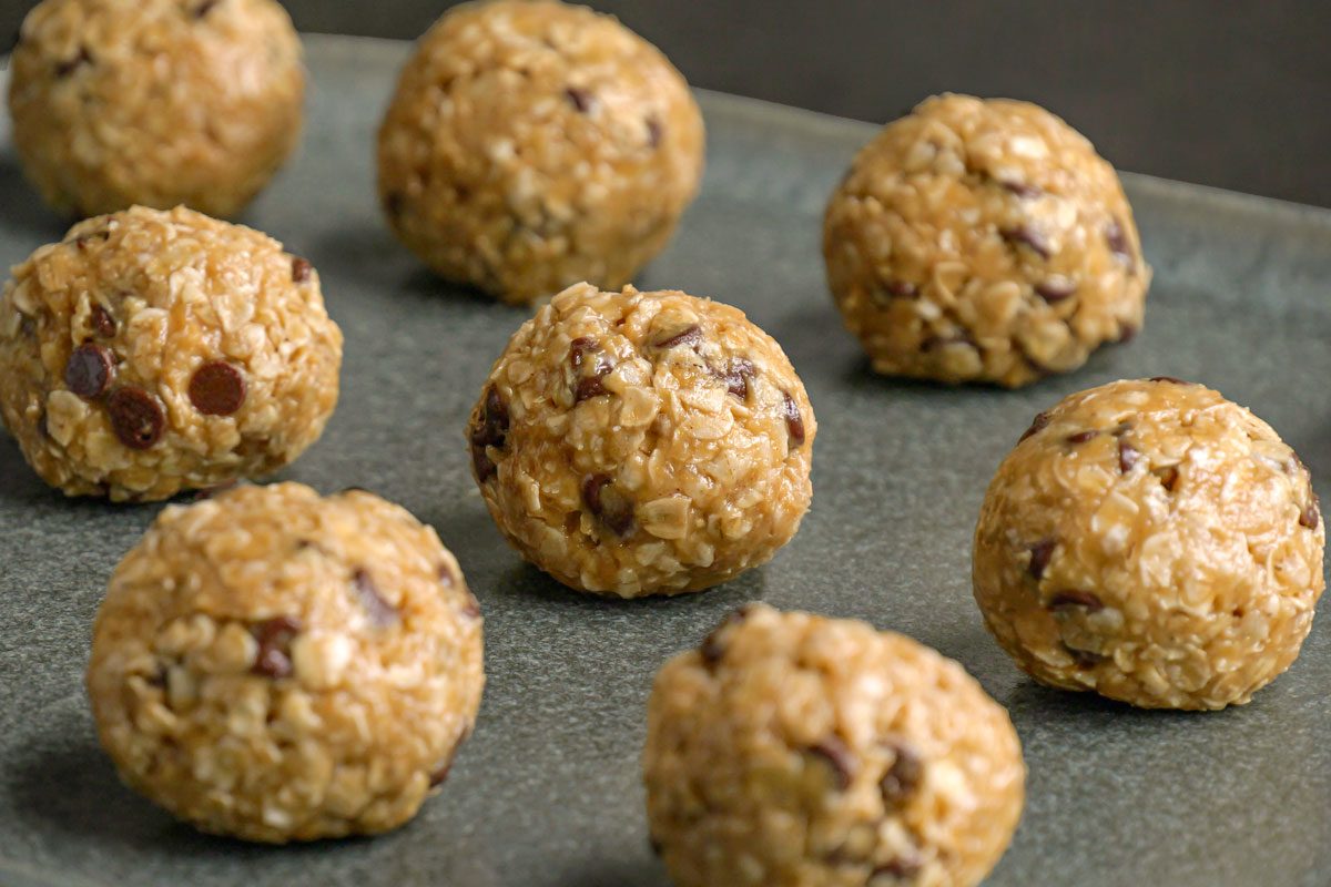Close-up shot of peanut butter oatmeal balls with chocolate chips, arranged on a gray rectangular tray; The textured oats and glossy chocolate flecks give the treats a rustic, homemade look;