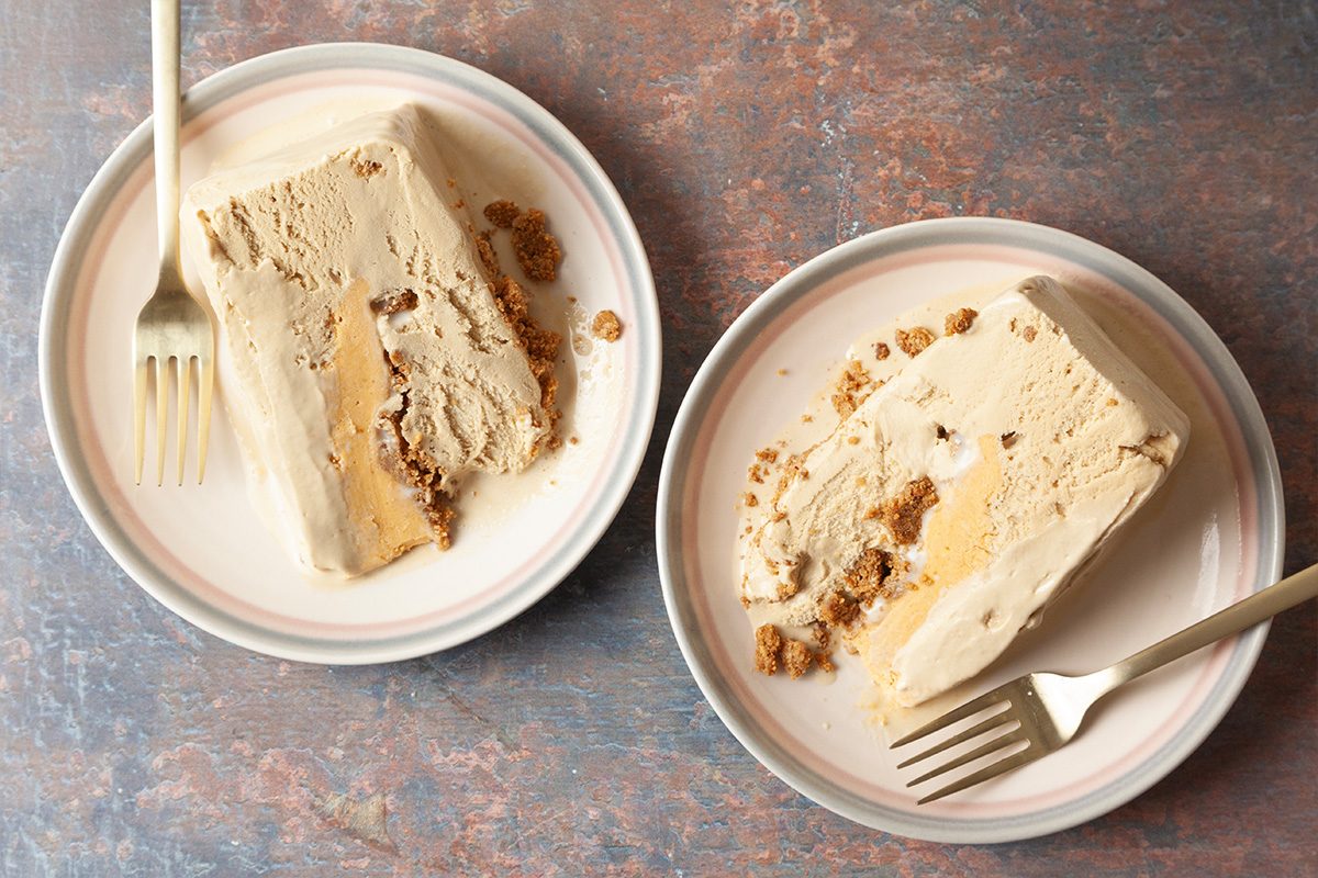 Two plates, each with a slice of creamy dessert that appears to have a crumbly filling or topping, are shown on a textured surface. Each plate has a fork placed next to the dessert.