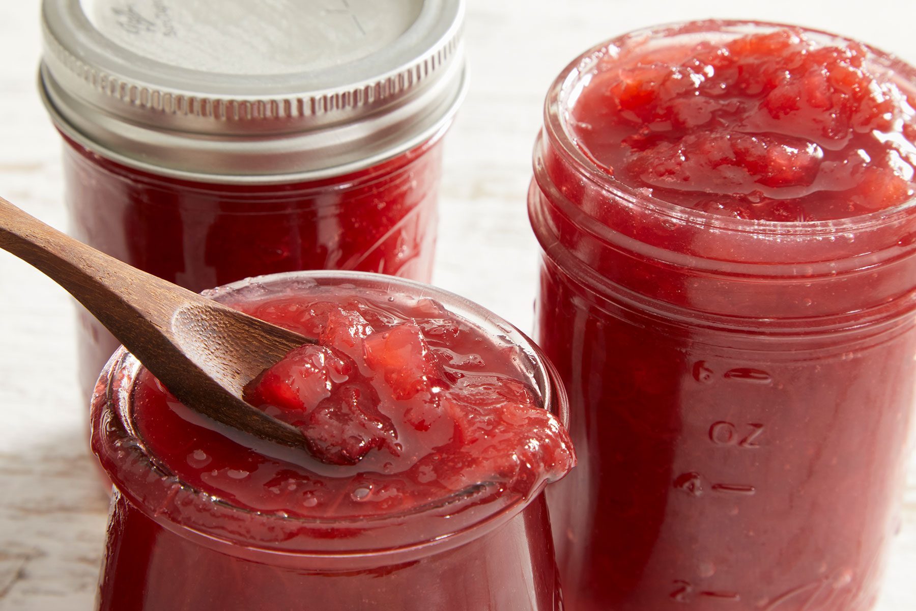 Rhubarb Pineapple Jam in glass jars with a wooden spoon dipped in one of them.