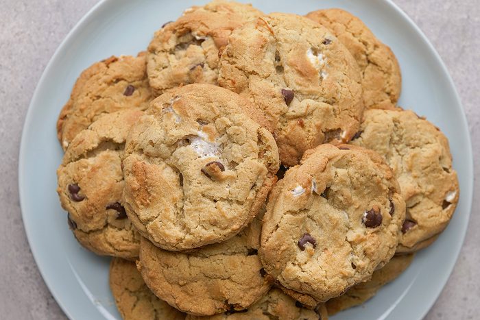 A plate of homemade chocolate chip cookies with a golden-brown color and slightly crisp edges, arranged in a pile on a light blue plate.