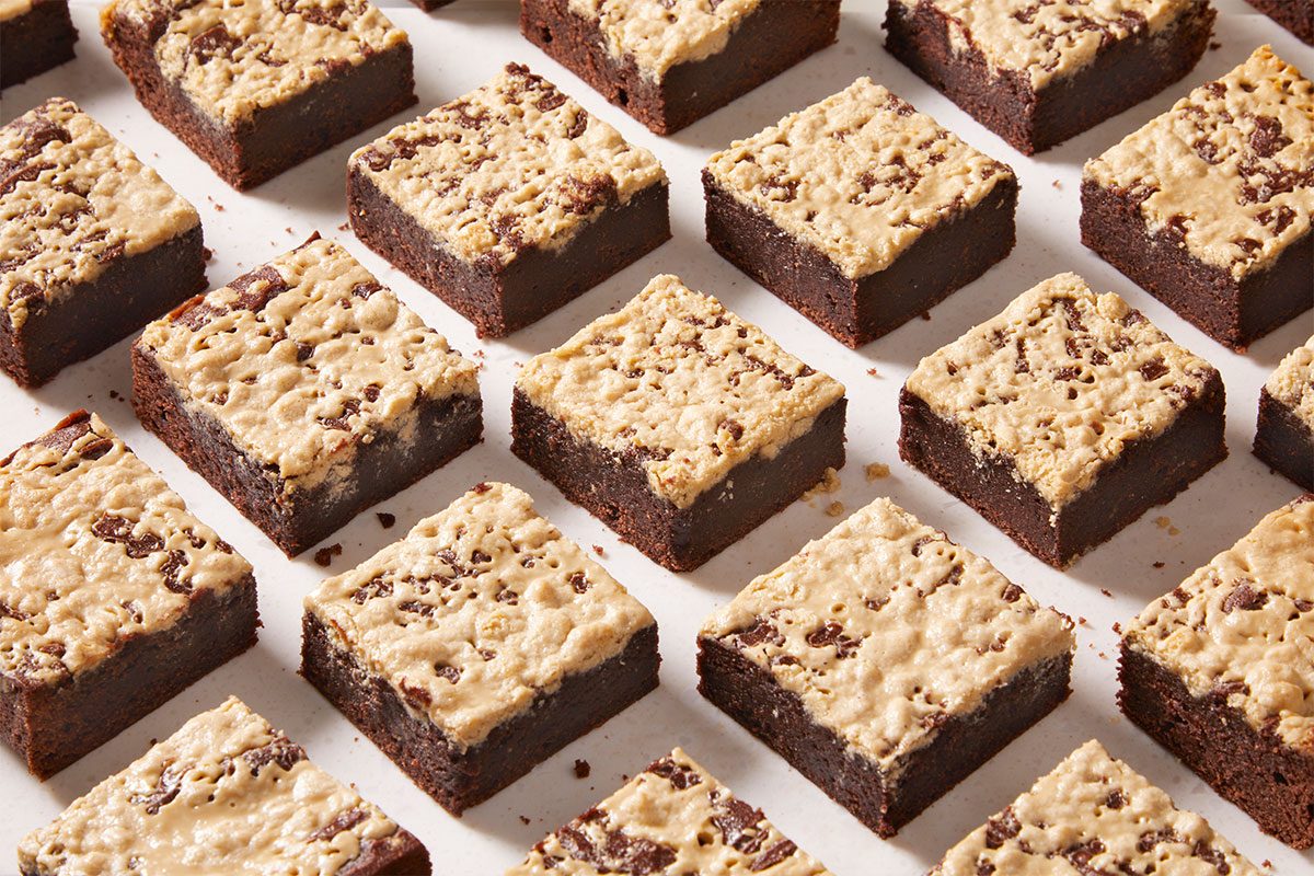 Rows of chocolate brownies topped with a light, crumbly layer are arranged neatly on a white surface. Each brownie square is evenly spaced, creating a grid-like pattern.