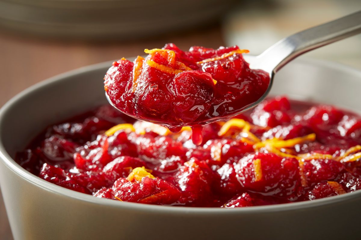 Close-up shot of a spoonful of Aperol Spritz Cranberry Sauce lifted from a bowl, garnished with vibrant orange zest;