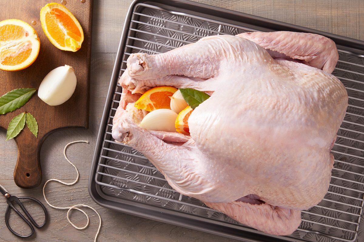 turkey stuffed with onion, orange and bay leaves next to chopping board with oranges