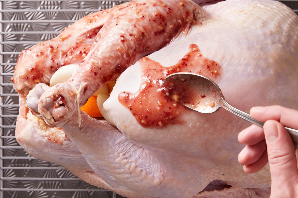 maple syrup, cranberry sauce and chopped walnuts mixture being spooned over turkey