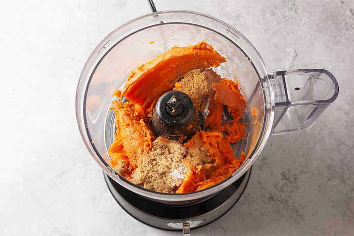 A food processor bowl filled with mashed sweet potatoes and a brown, crumbly ingredient, viewed from above on a light gray countertop.
