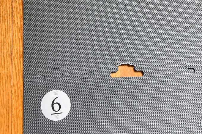 A textured gray panel with a puzzle-like connection slot and a piece missing, revealing a wooden surface beneath. A white circle with the number 6 is in the lower left corner of the panel.