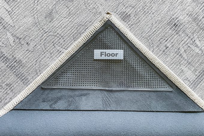 A close-up of the corner of a rug lifted to reveal a triangular label underneath with the word “Floor” printed on it, indicating which side should face down.
