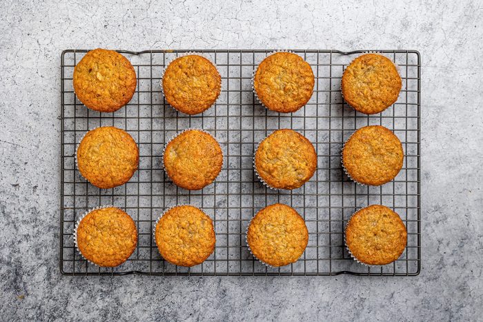 Overhead shot of twelve golden-brown muffins arranged in rows on a wire cooling rack, set on a gray textured surface