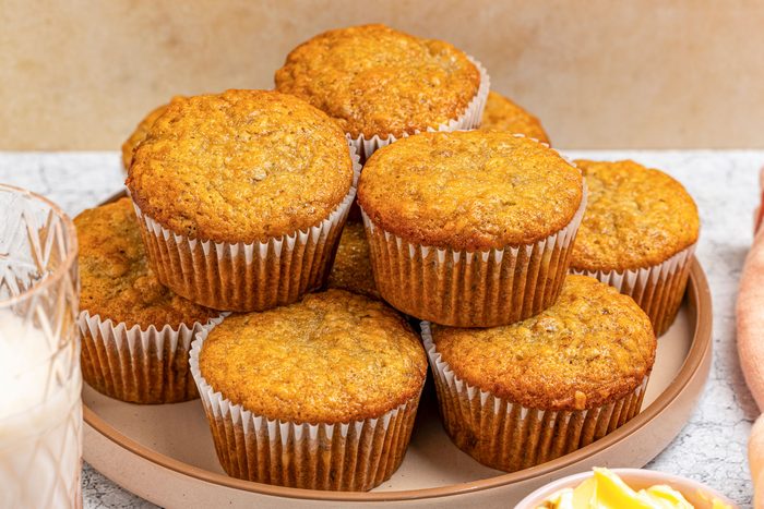 Close-up shot of vegan banana muffins stacked on a round tray; each in a white paper liner; placed on a gray surface
