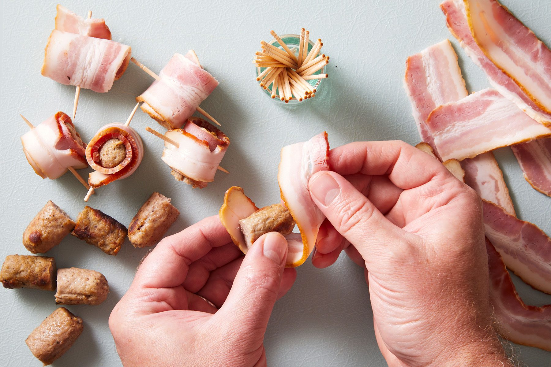 Wrapping a piece of bacon around each piece of sausage.