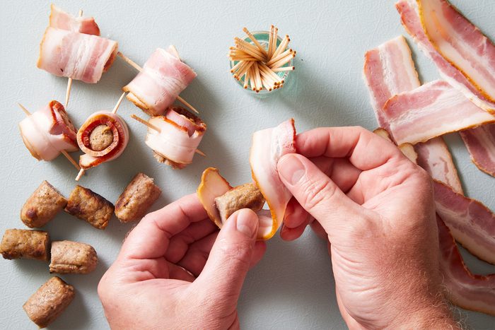 Wrapping a piece of bacon around each piece of sausage.