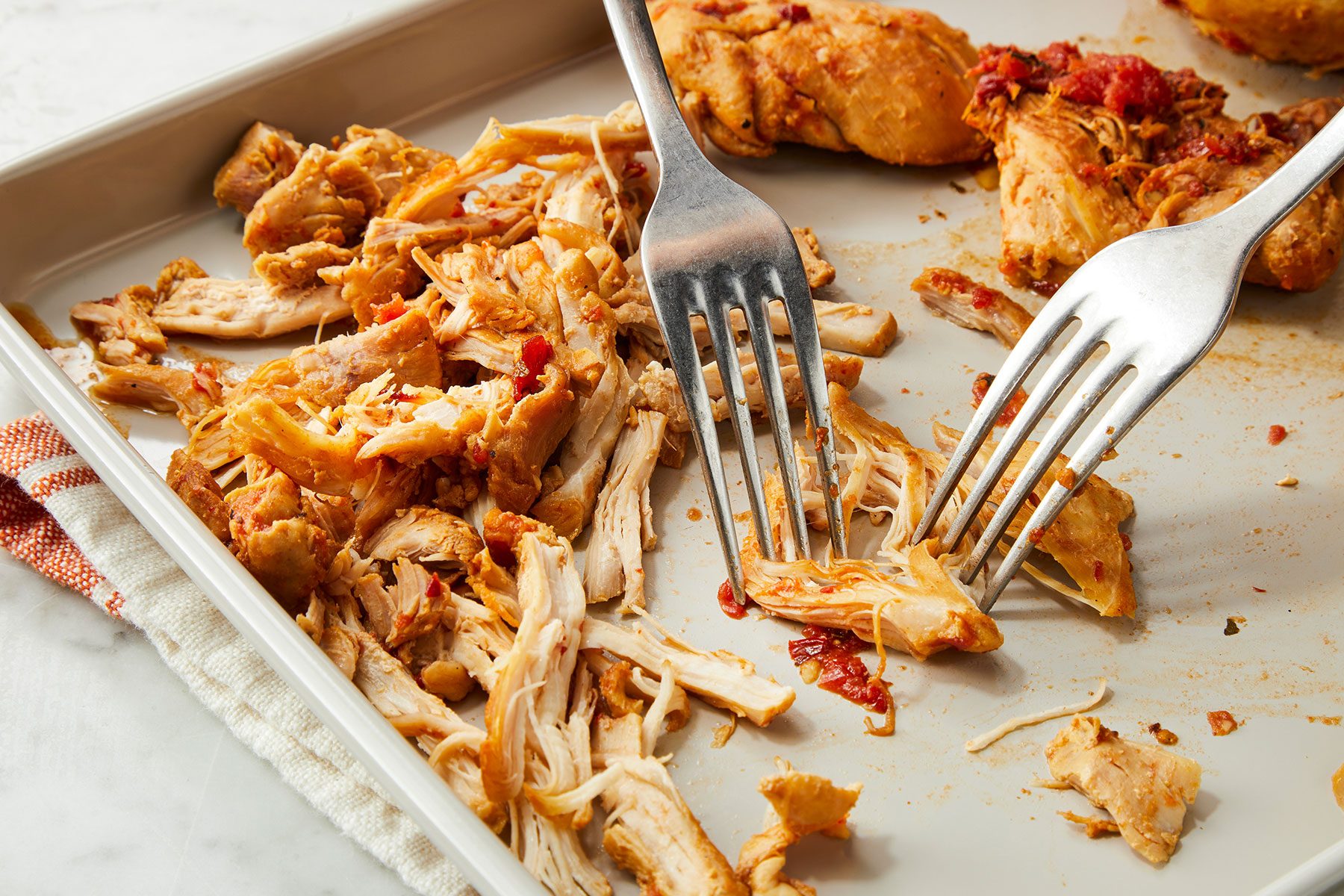 Shredding the cooked chicken using two forks in a dish.