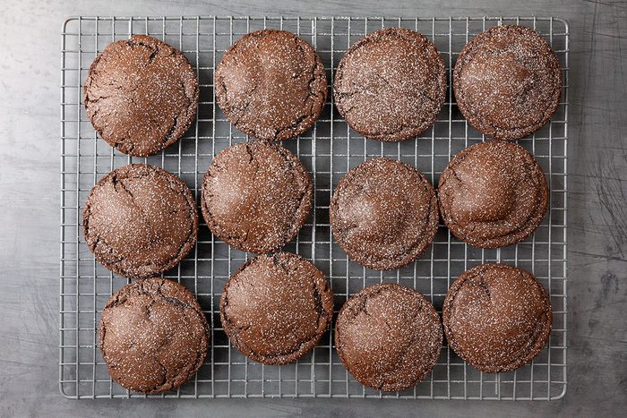 Overhead shot of Chocolate Lava Cookies are arranged in twelve neat rounds on a metal cooling rack on a gray surface they are dusted with sugar