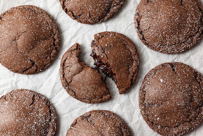 Close-up shot of Chocolate Lava Cookies are laid out on parchment paper and dusted with powdered sugar one cookie in the center is split open showing a gooey inside