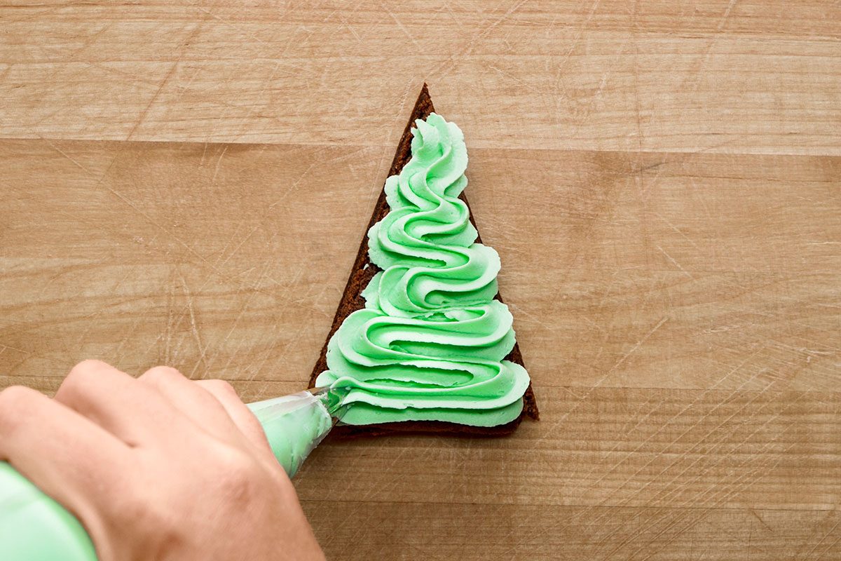 adding frosting to the brownies using a pipe for Christmas Tree Brownies