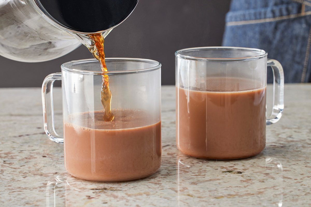 Overhead shot of a person pouring coffee into a clear glass mug filled with chocolate milk