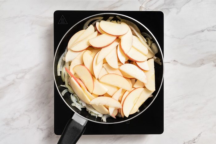 Overhead shot of placing apples on top of onions; induction; all set on a marble surface;