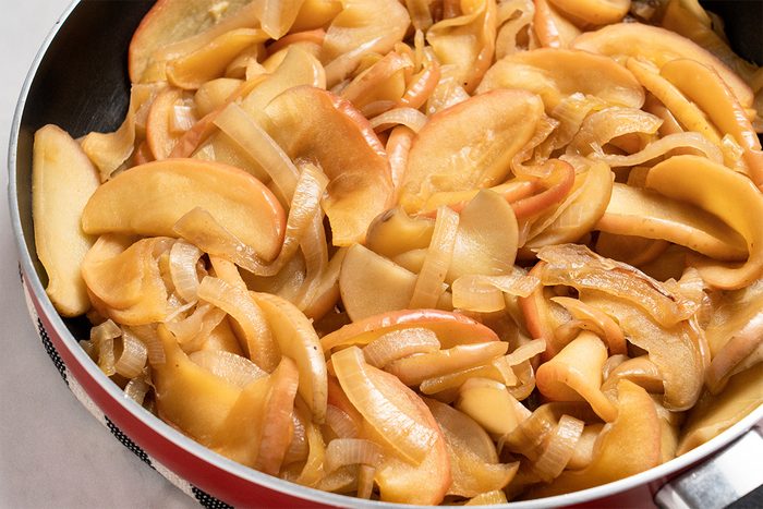 Close up shot of Fried Onions and Apples in the skillet; all set on a white marble surface;