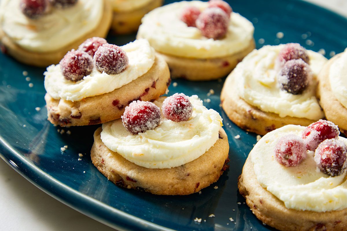 Close-up shot of Frosted Sugared Cranberry Cookies topped with sugared cranberries on a teal plate.
