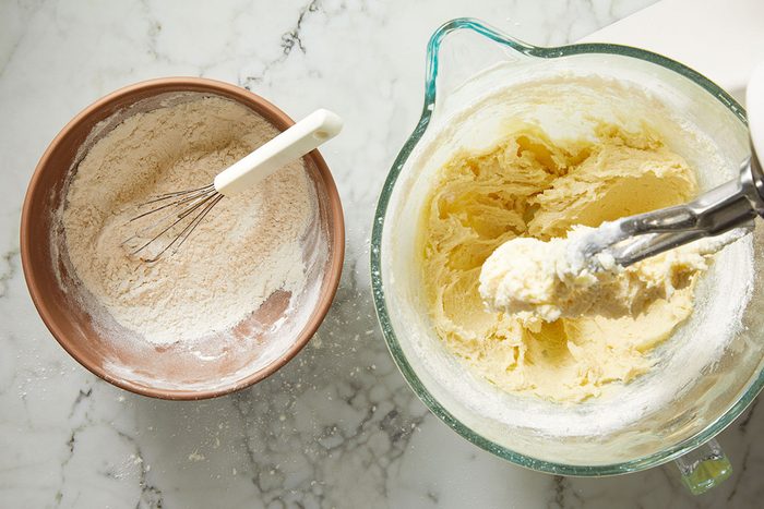 Overhead shot of mixing dry ingredients into the creamed butter mixture on a marble surface.