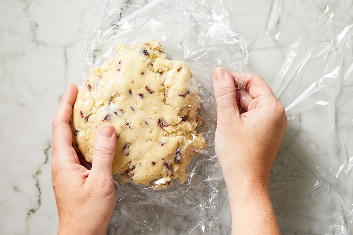 Overhead shot of cookie dough being shaped into a log and wrapped in plastic wrap.