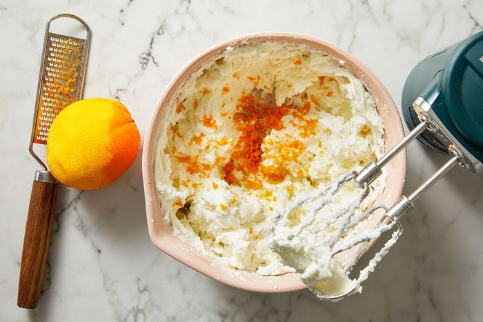Overhead shot of orange zest being mixed into frosting in a small bowl with a whisk.