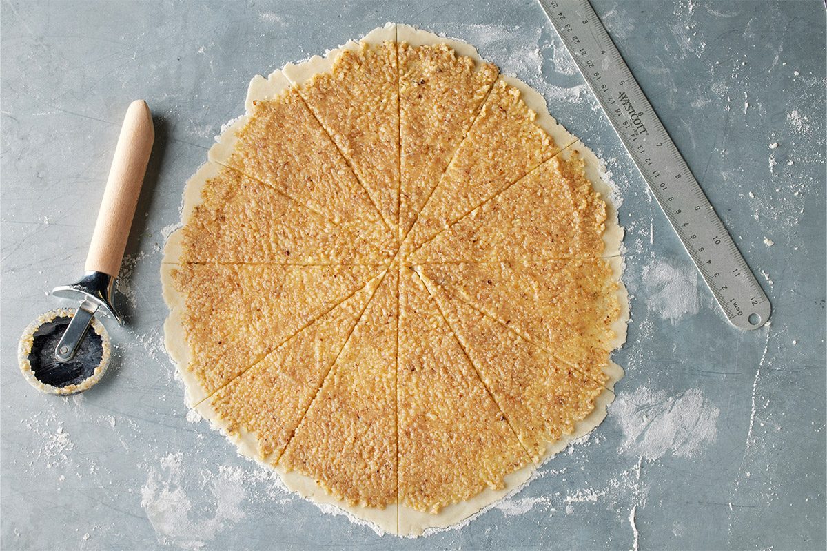 Overhead shot of a round sheet of dough with filling, divided into triangles on a floured surface, with a pastry cutter and ruler nearby;