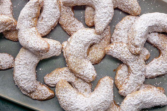3/4th Shot of Pecan Crescent Cookies; A platter shows crescent-shaped cookies covered in powdered sugar arranged neatly on a rectangular plate they slightly overlap each other