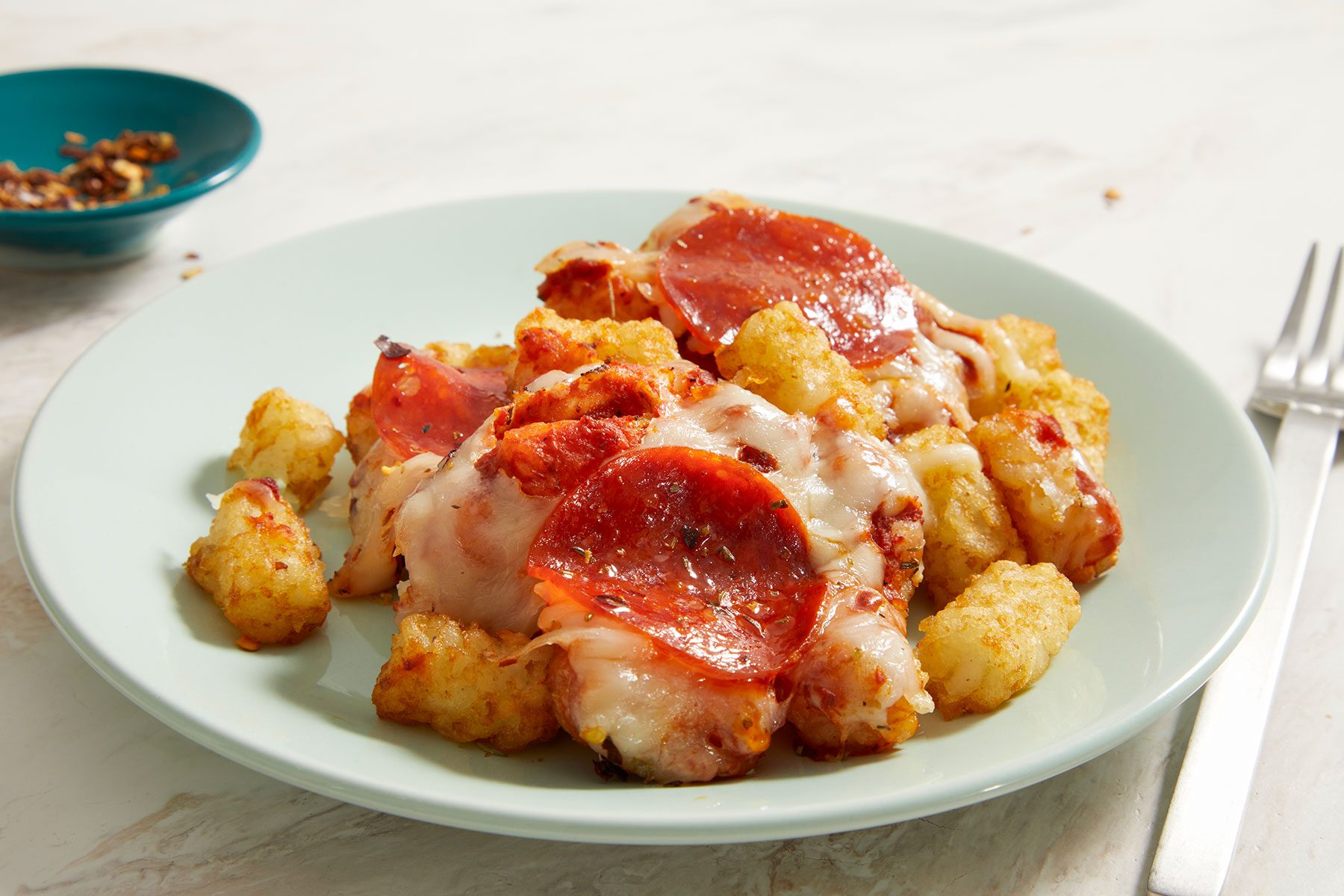 Pizza Tots served in a small dish with a fork and pepper flakes kept on side.