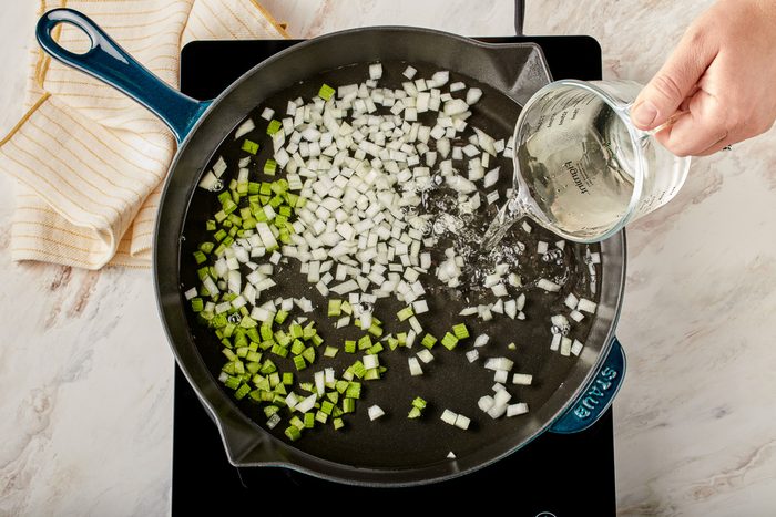 adding water to onion and celery in a skillet