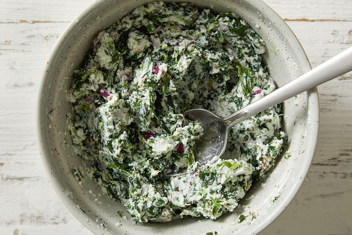 Overhead shot of a white bowl filled with a creamy ricotta and spinach mixture with a spoon resting inside