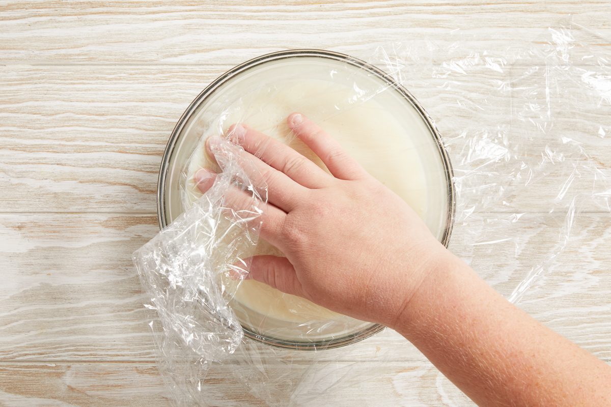 plastic wrap being pressed onto surface of bowl with frosting mixture