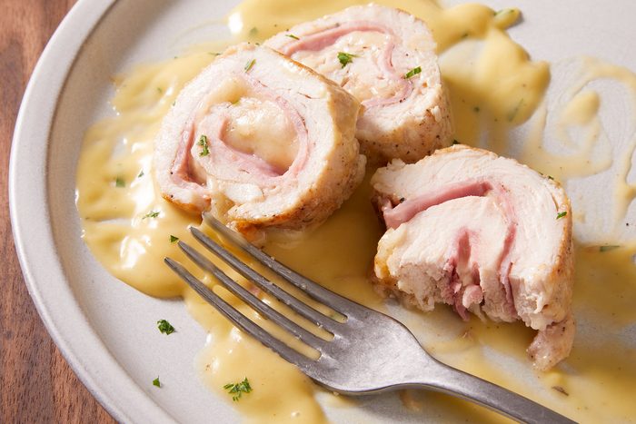 Stuffed Chicken Rolls with garnishing of parsley and a fork on a white plate.