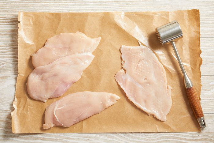 Overhead shot of raw chicken breasts placed on parchment paper beside a meat mallet on a light surface.