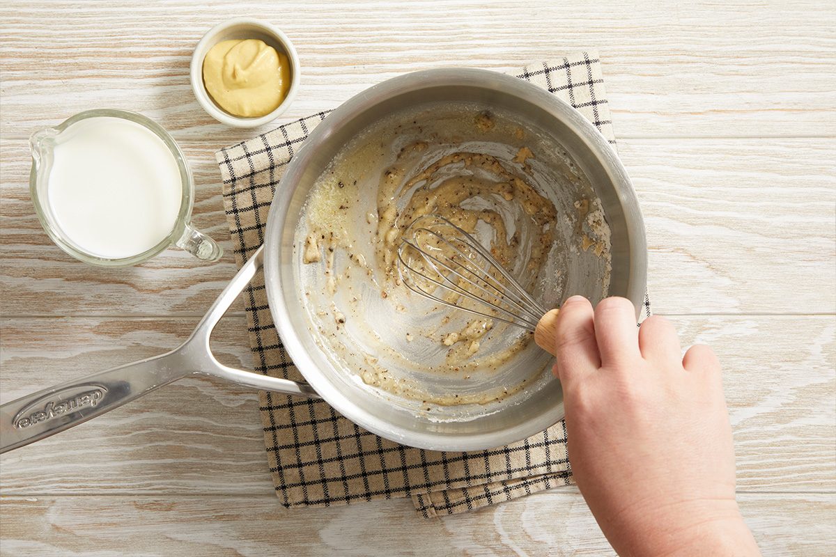 Overhead shot of a saucepan with melted butter being whisked to prepare sauce for the sandwich.