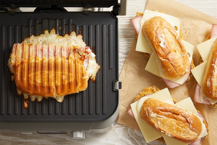 Overhead shot of Chicken Cordon Bleu Sandwich grilling on a panini press with cheese melting inside.