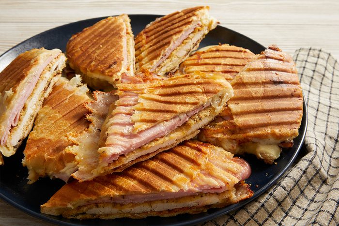 Overhead shot of multiple Chicken Cordon Bleu Sandwich halves stacked on a plate with grill marks visible.