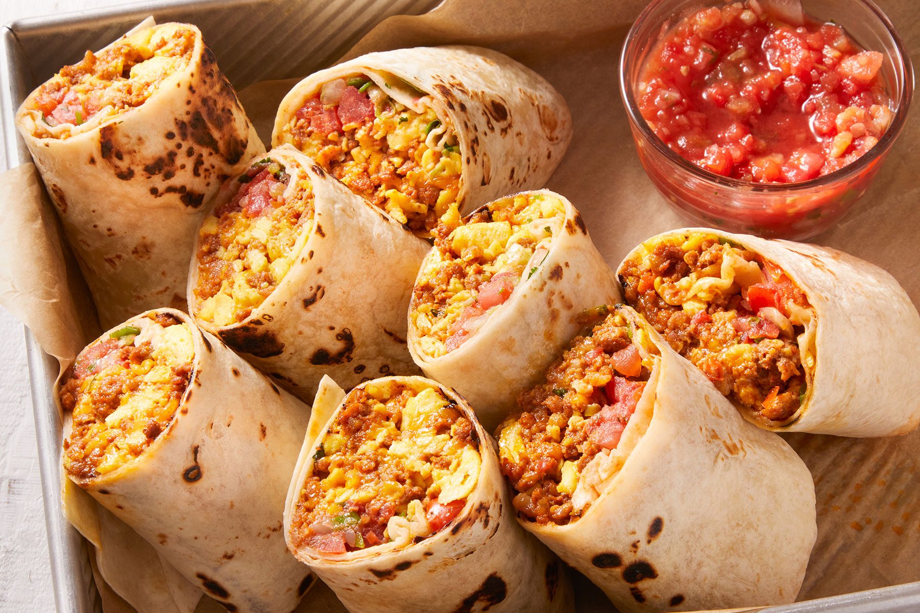 Chorizo Egg Wraps cut into halves and diced tomatoes in a small bowl on side.