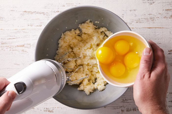 Beating eggs into butter and sugar mixture in a bowl to bake a cake.