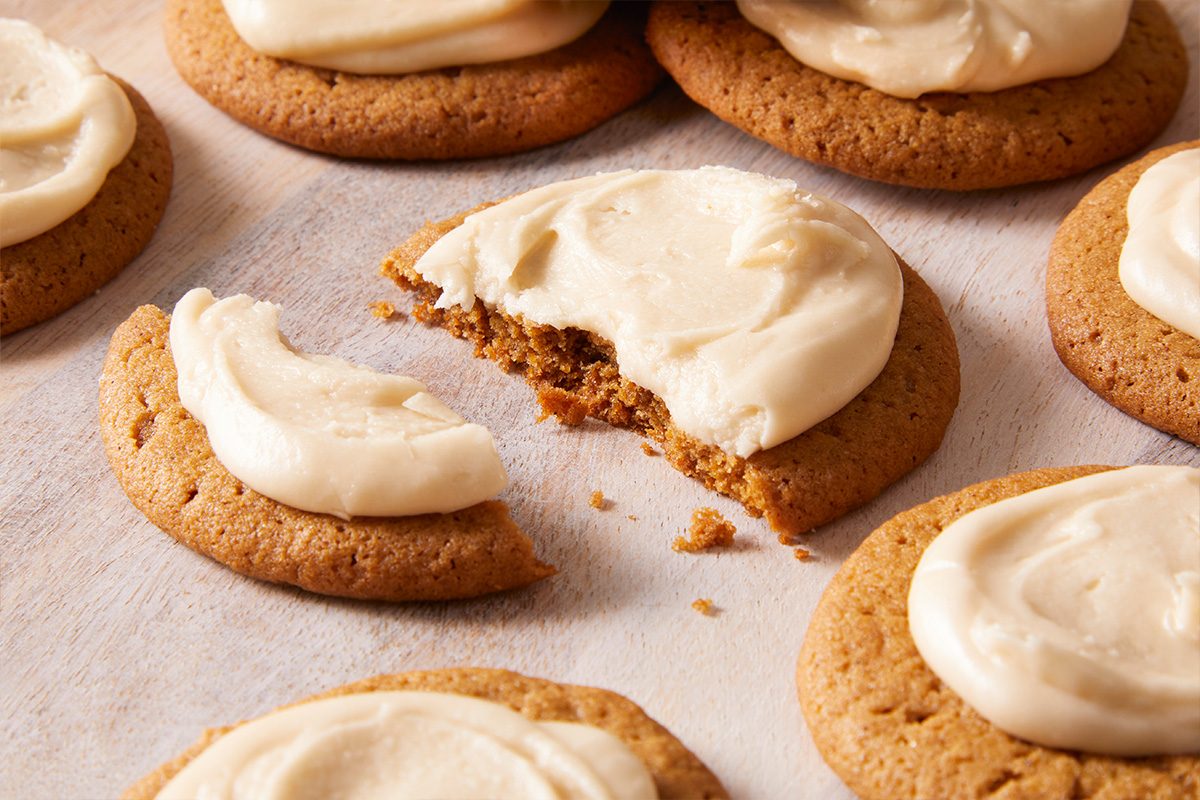 Close-up shot of Frosted Ginger Cookies on parchment paper with one cookie broken in half to show the soft texture inside.