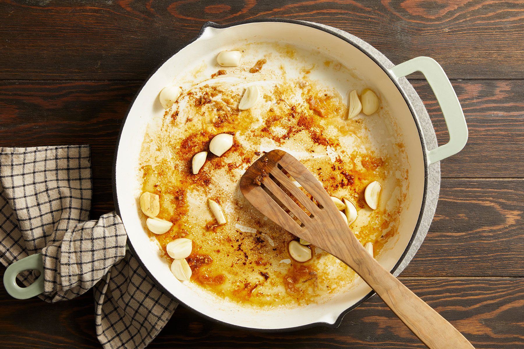 Adding halved garlic cloves along with the brandy or chicken stock to a large warm skillet.