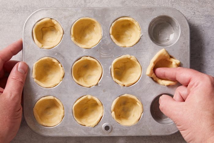 Gently pressing each dough piece into the bottom and up the sides of greased miniature muffin cups.