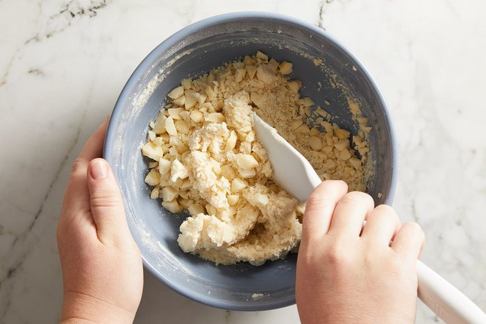 Overhead shot of hands mixing crushed nuts in a blue bowl with a white spatula.