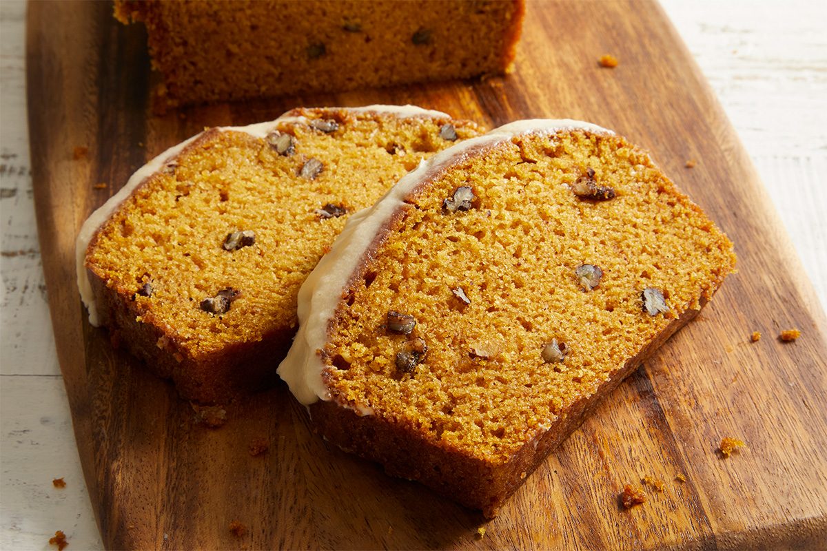 Two slices of moist pumpkin bread with nuts and a light glaze on top, resting on a wooden cutting board.