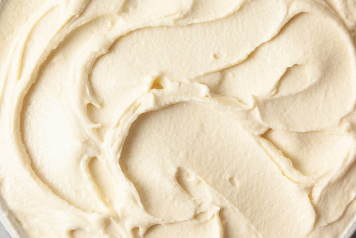 Closeup shot of smooth Russian buttercream swirled into soft, creamy waves, its light, velvety texture shown through subtle ridges and curves in a pale ivory tone;