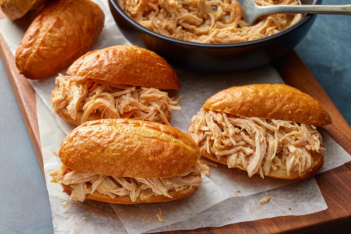 3/4 angle view shot of slow-cooker shredded turkey sandwiches on a wooden board